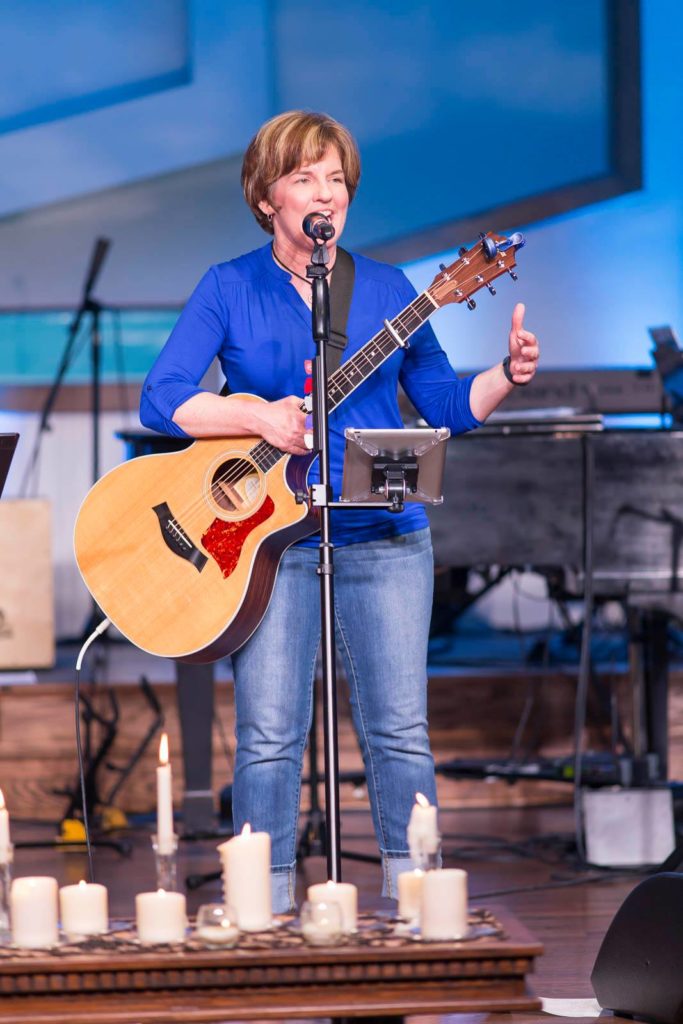 Kelly crane speaking into a microphone on stage. She's holding her guitar, ready to rock.