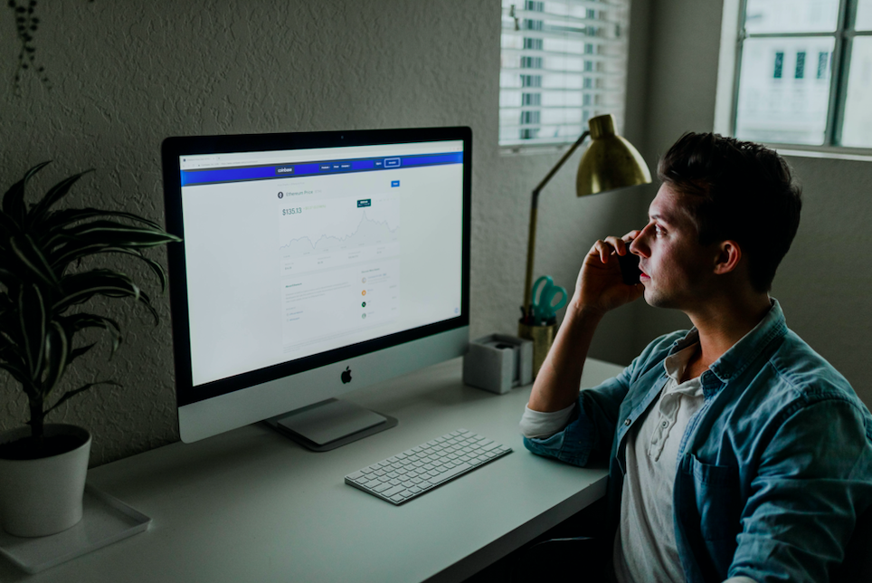 Man sitting at a desk, viewing a mac desktop that is open to an unknown website.