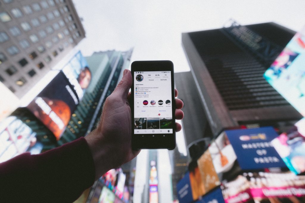 A man holding up a cell phone open to the Instagram app with skyscrapers in the background.