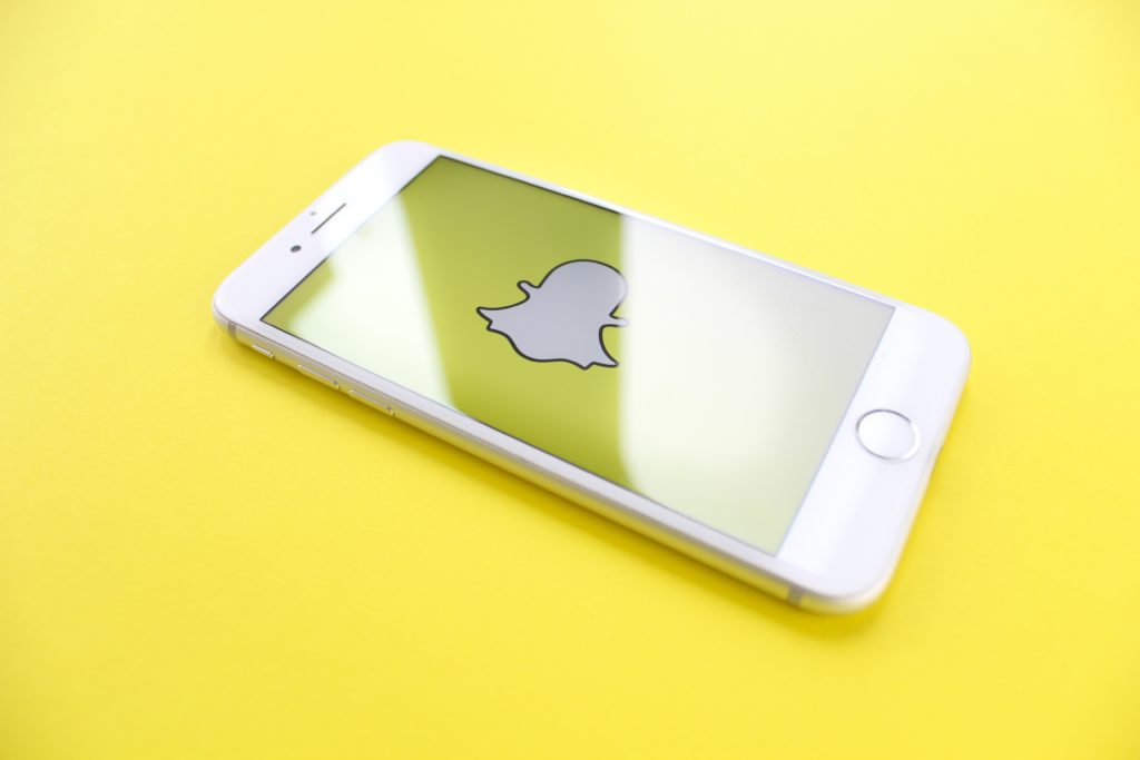 An iPhone displaying the Snapchat logo on a yellow background.