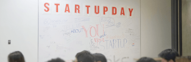A room full of people in front of a board that reads, "Startupday."