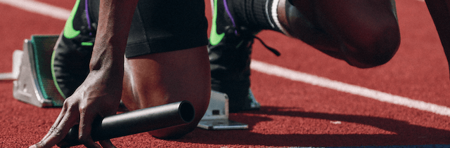 A male runner at the start line, holding a baton.