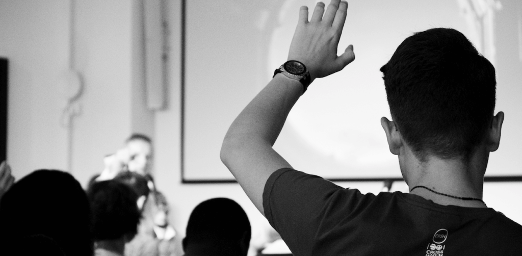 A young man in an audience raising his hand.