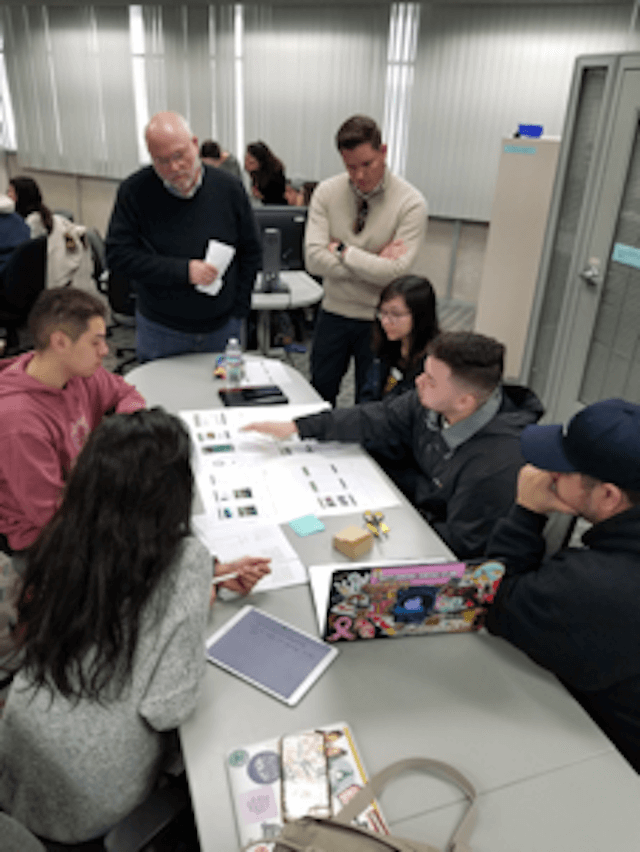 Students and alumni around a table, discussing mobile app designs