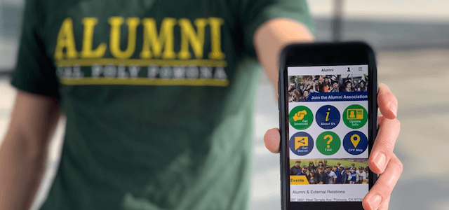 A man wearing a Cal Poly Pomona alumni T-shirt and holding a mobile phone that is displaying the new alumni association app. 