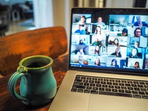 An image of a laptop on a table open to a Zoom video chat meeting. There is a coffee mug to the left of the laptop. 