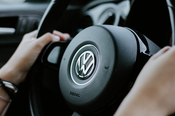 Person gripping Volkswagen car steering wheel.