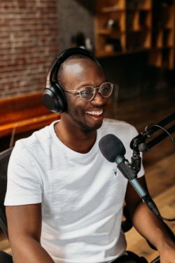 A young man sitting at a desk with headphones on and speaking into a microphone.